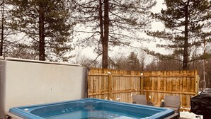 Un jacuzzi en un patio trasero con valla de madera y árboles al fondo.