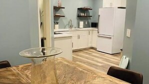 Una cocina compacta con armarios blancos, un refrigerador blanco y una mesa de comedor con un centro de mesa de vidrio.