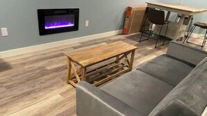 Una sala de estar con un sofá gris, una mesa de centro de madera y un televisor montado en la pared.
