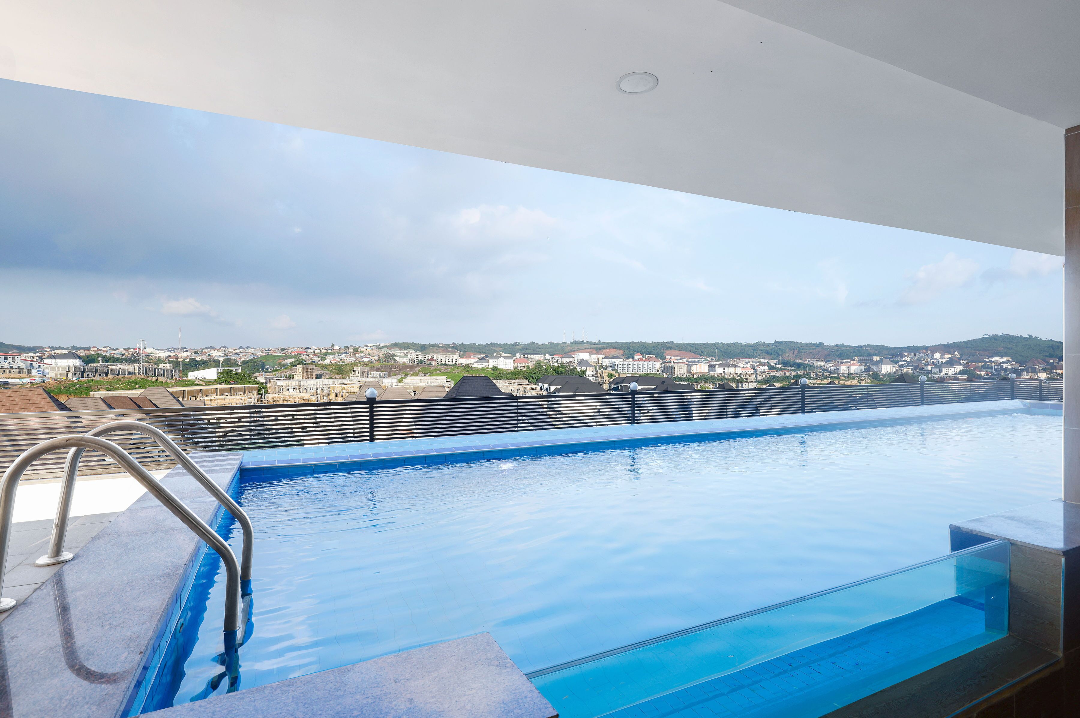 A rooftop infinity pool with a metal railing and a clear view of the cityscape in the background.