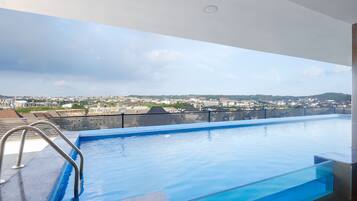 A rooftop infinity pool with a metal railing and a clear view of the cityscape in the background.