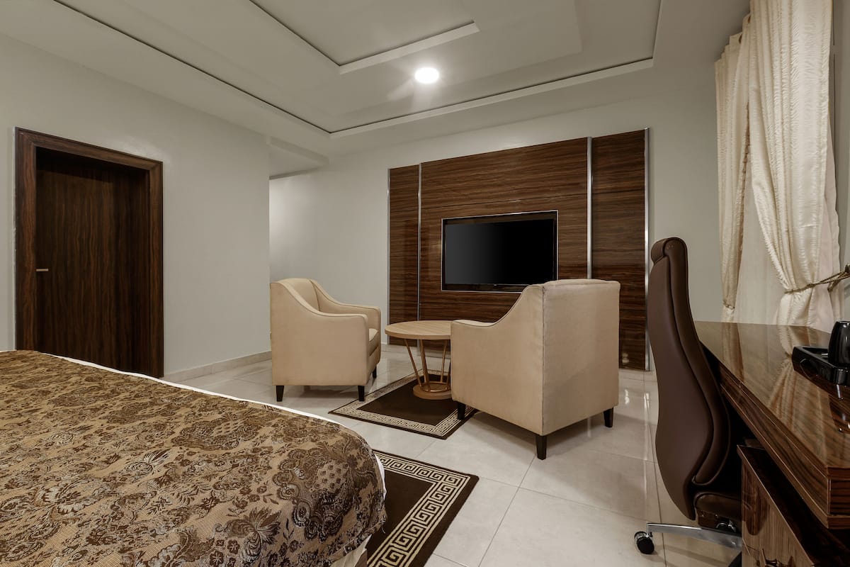 Habitación de hotel con una cama, dos sillones, una mesita redonda, un televisor montado en una pared de paneles de madera y un escritorio con una silla.