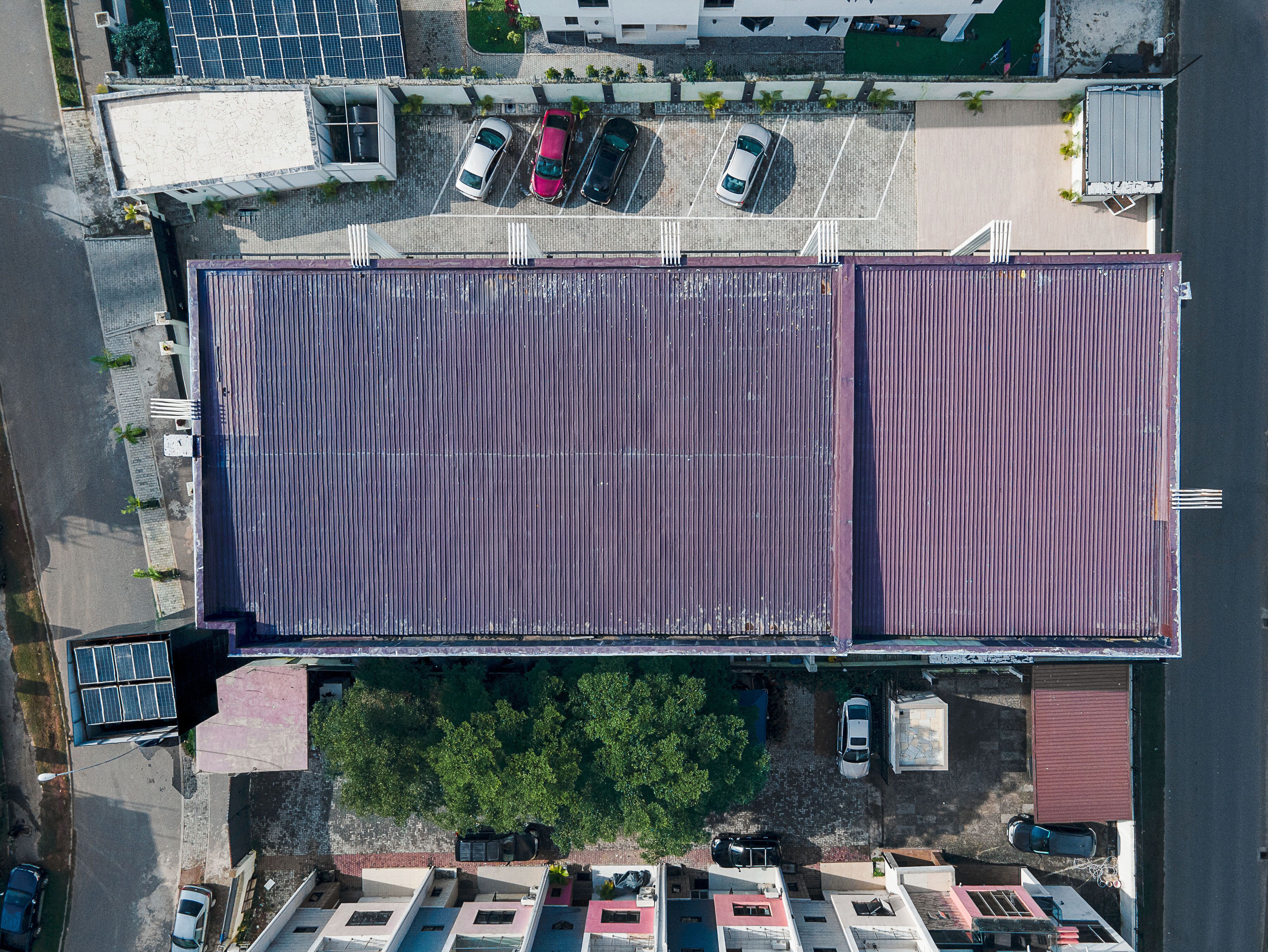 An aerial view of a parking lot with several cars, a building with a red roof, and a green area with trees.
