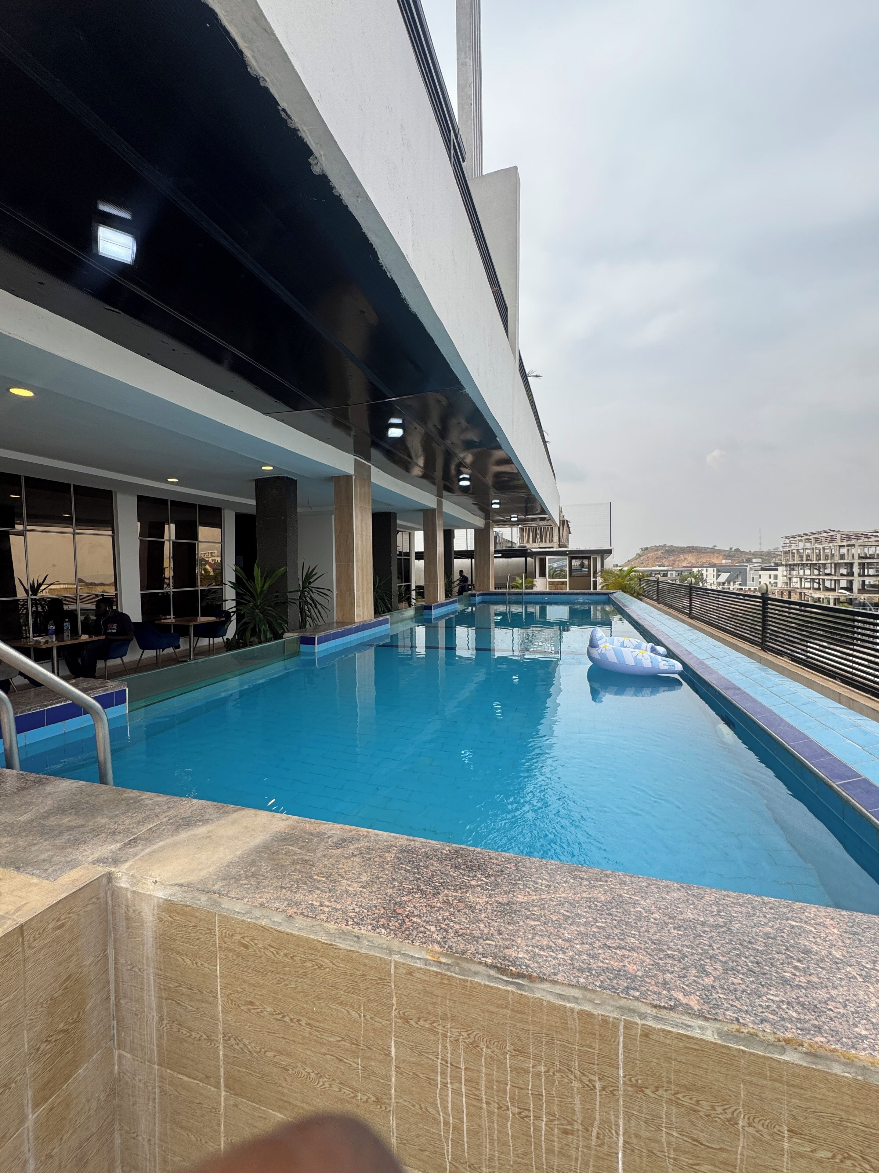 An indoor swimming pool with clear blue water, surrounded by a tiled deck and a railing.