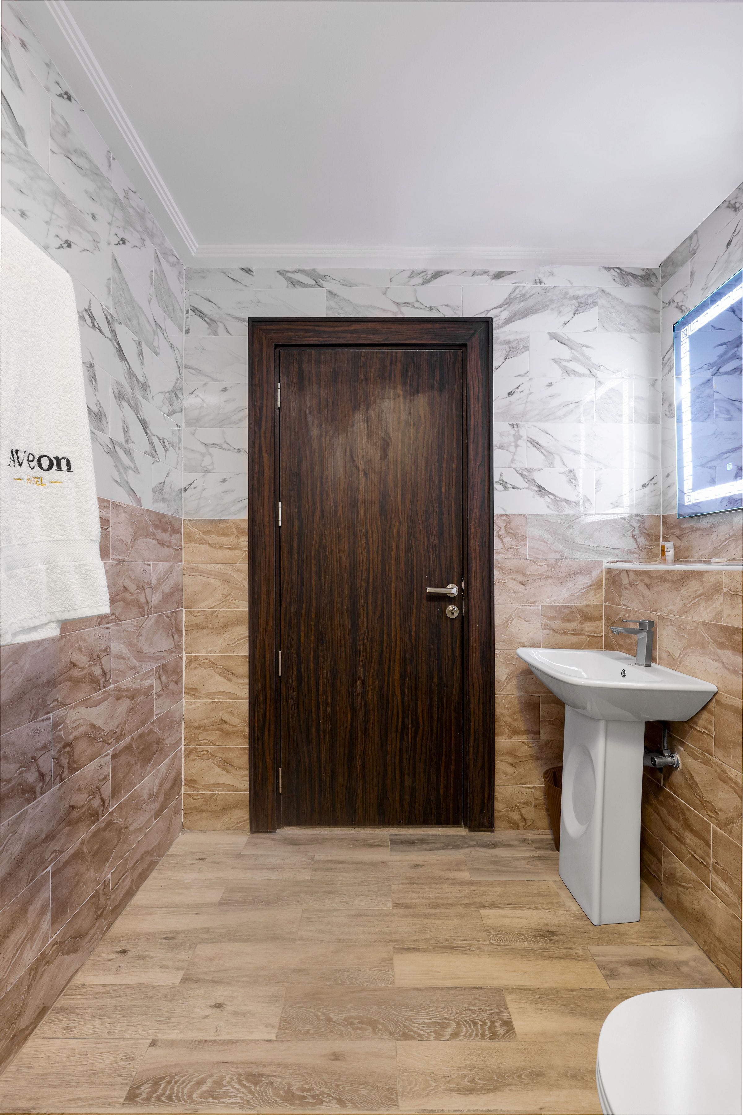 Un baño con paredes de mármol, una puerta de madera, un lavabo y un inodoro.