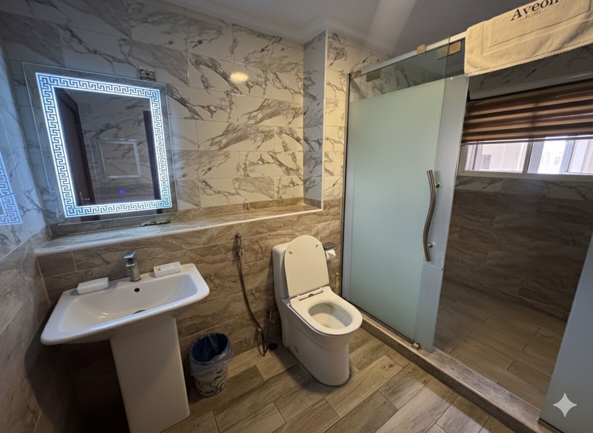 A bathroom with a marble wall, a sink, a toilet, and a glass shower enclosure.