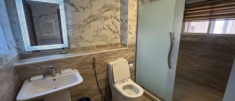 A bathroom with a marble wall, a sink, a toilet, and a glass shower enclosure.