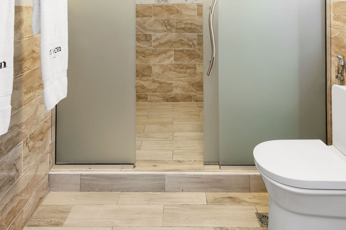Un baño moderno con ducha envuelta en vidrio, paredes de mármol y un inodoro blanco.