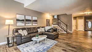 Ein modernes Wohnzimmer mit einem dunkelbraunen Ledersofa, einem weißen Couchtisch und einem gemusterten Teppich. Eine Treppe führt zu einer weiteren Ebene, und im Hintergrund ist eine Tür sichtbar.
