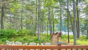 Eine Holzterrasse mit Adirondack-Stühlen, die auf einen Wald und einen See blickt.