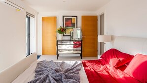 Un dormitorio moderno con cama, mesita de noche, lámpara y cómoda.