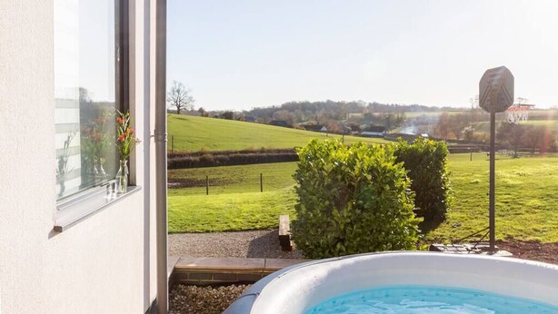 Vista desde una ventana sobre un paisaje verde con una piscina al frente.