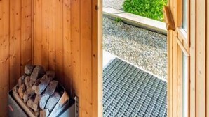 Interior de una cabaña de madera con chimenea, una puerta que da al exterior y vistas a un paisaje verde.