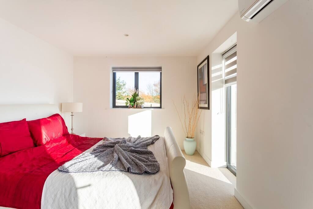 Une chambre à coucher avec un lit, une fenêtre, une plante en pot et un climatiseur fixé au mur.