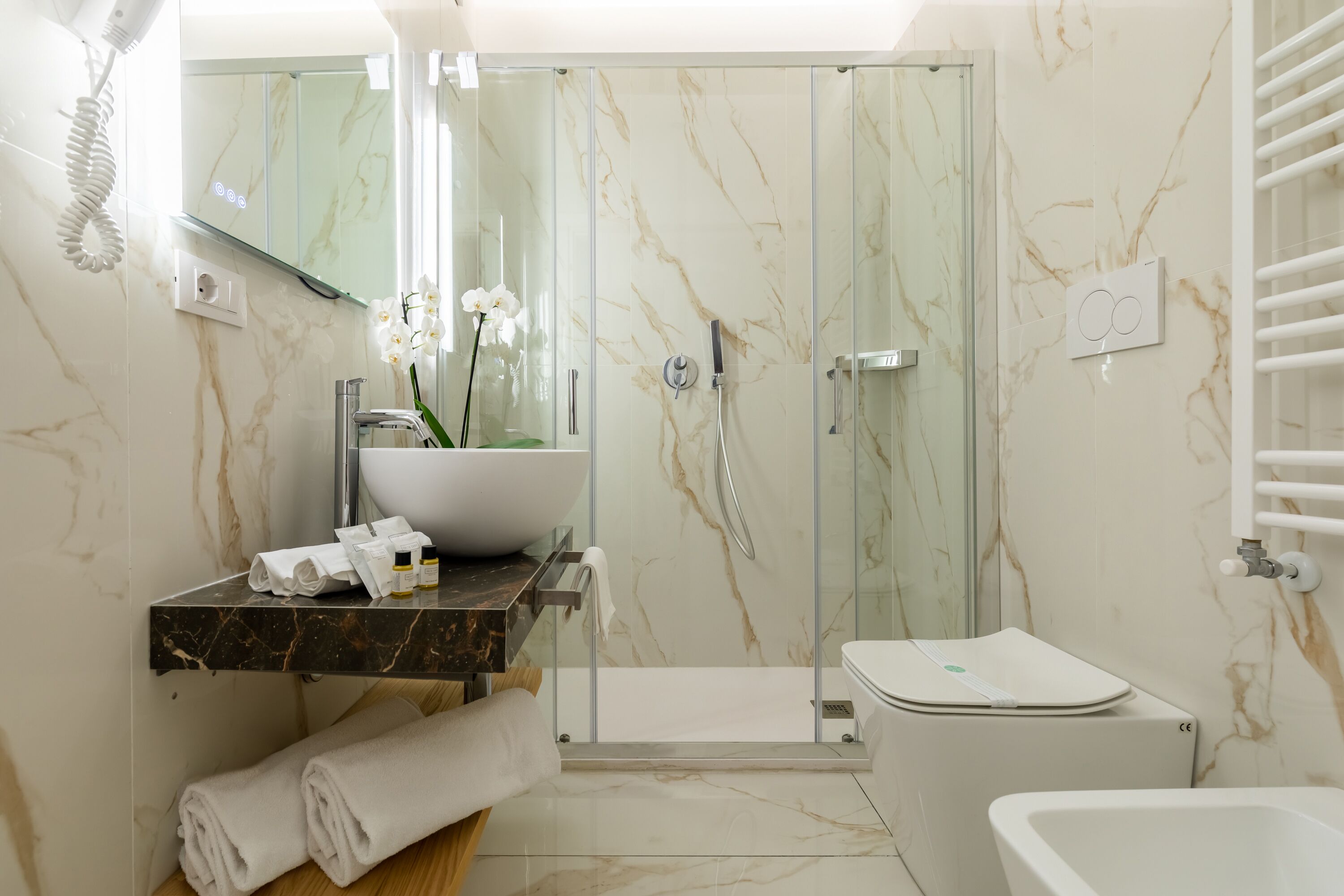 A modern bathroom with a glass-enclosed shower, a white sink, and a marble-tiled wall.