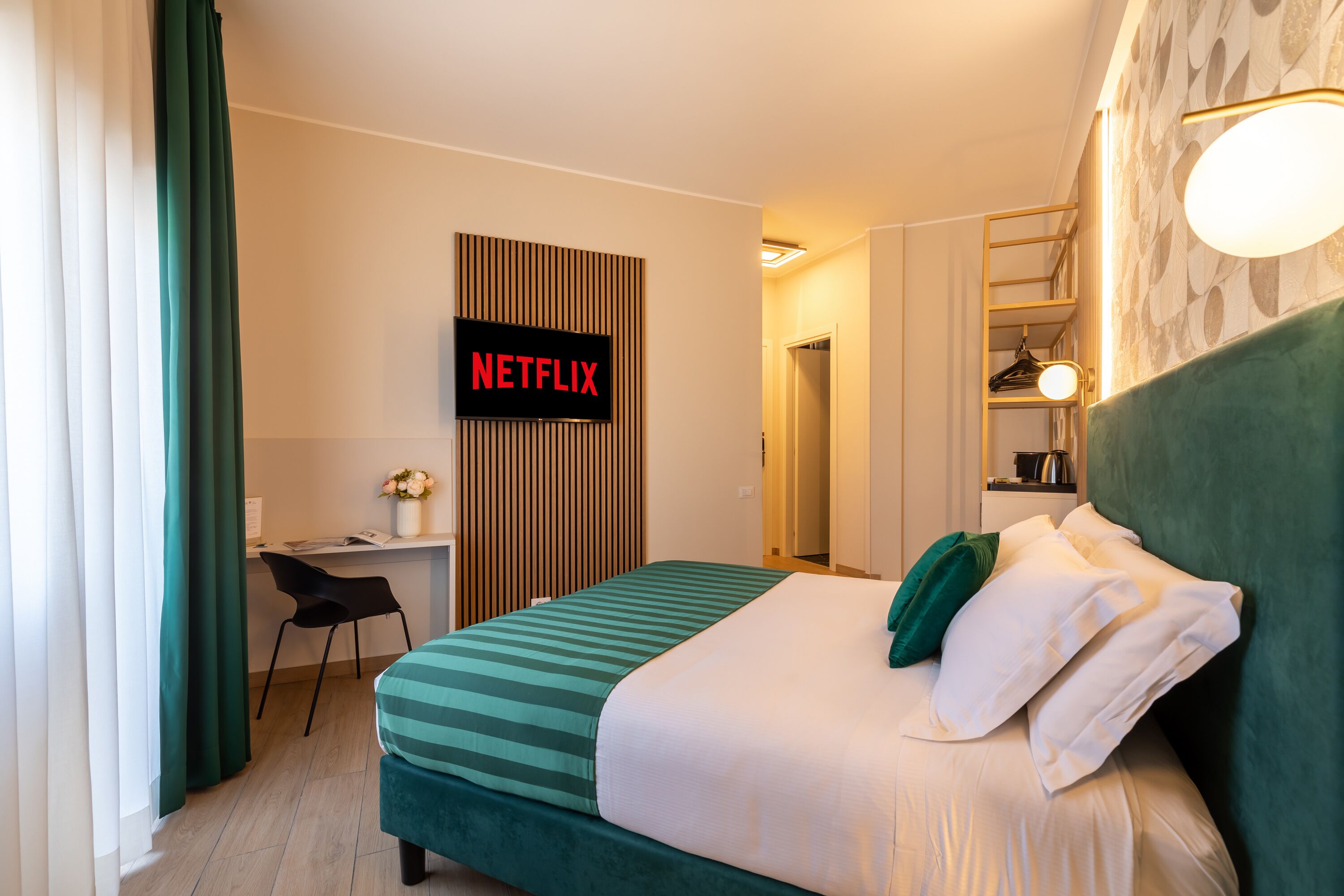 A hotel room with a bed, a desk, a chair, a TV displaying "NETFLIX", and a wardrobe.