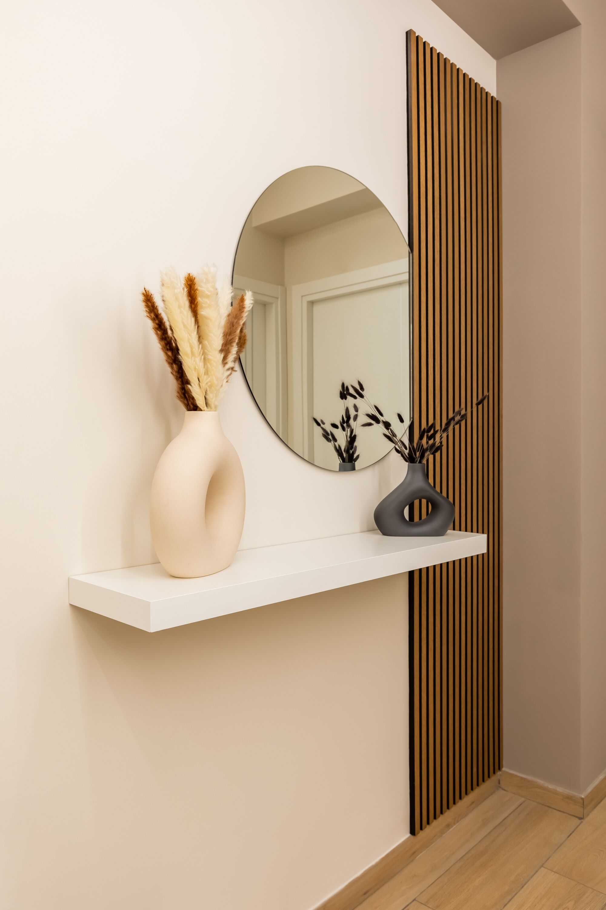 A white console table with two vases containing pampas grass, positioned in front of a mirror and a vertical wooden panel.