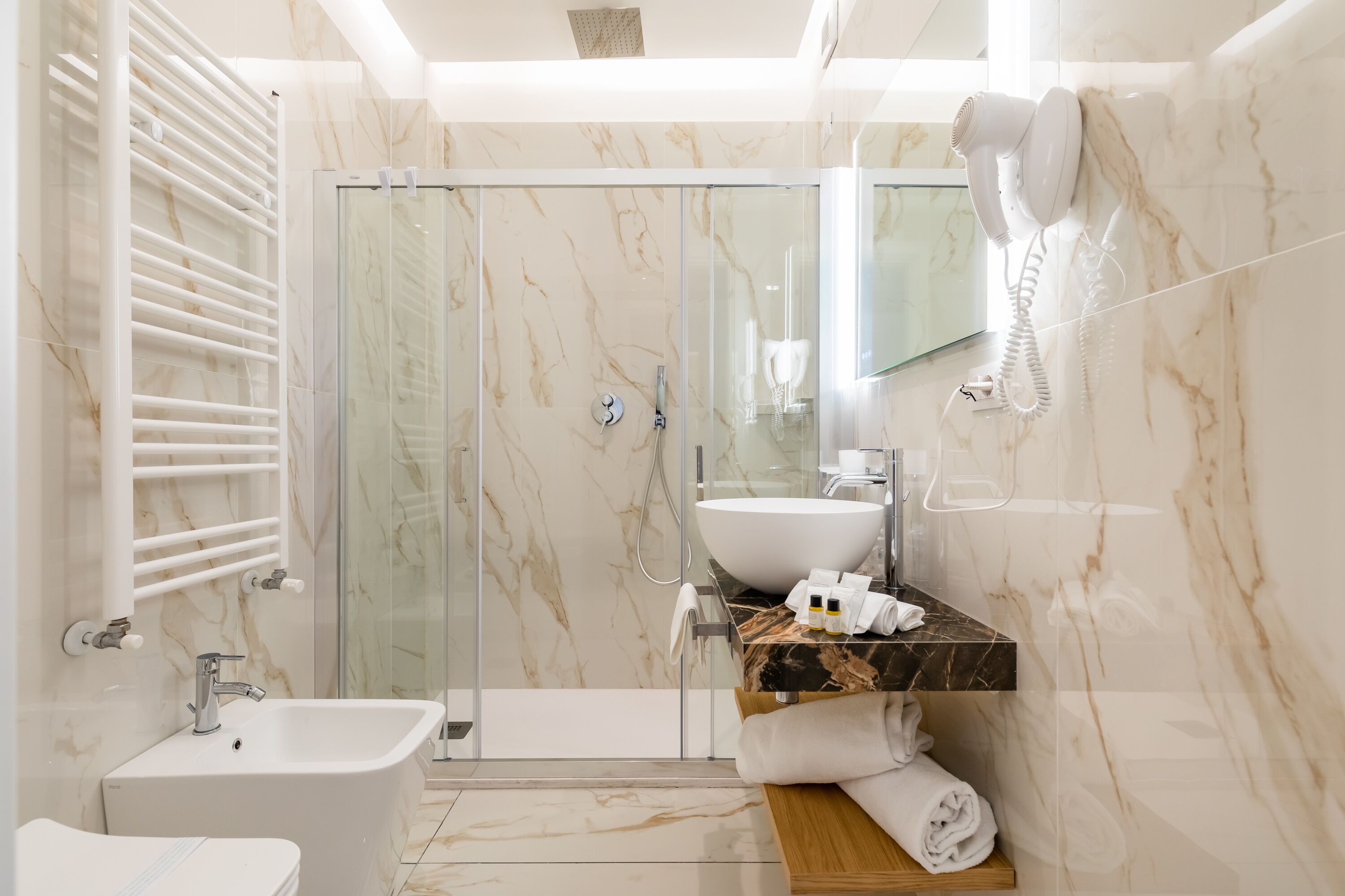 A modern bathroom with a glass-enclosed shower, a white sink, and a hairdryer mounted on the wall.