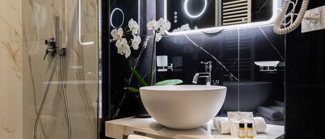 A modern bathroom with a glass-enclosed shower, a white sink, and a hairdryer on the wall.