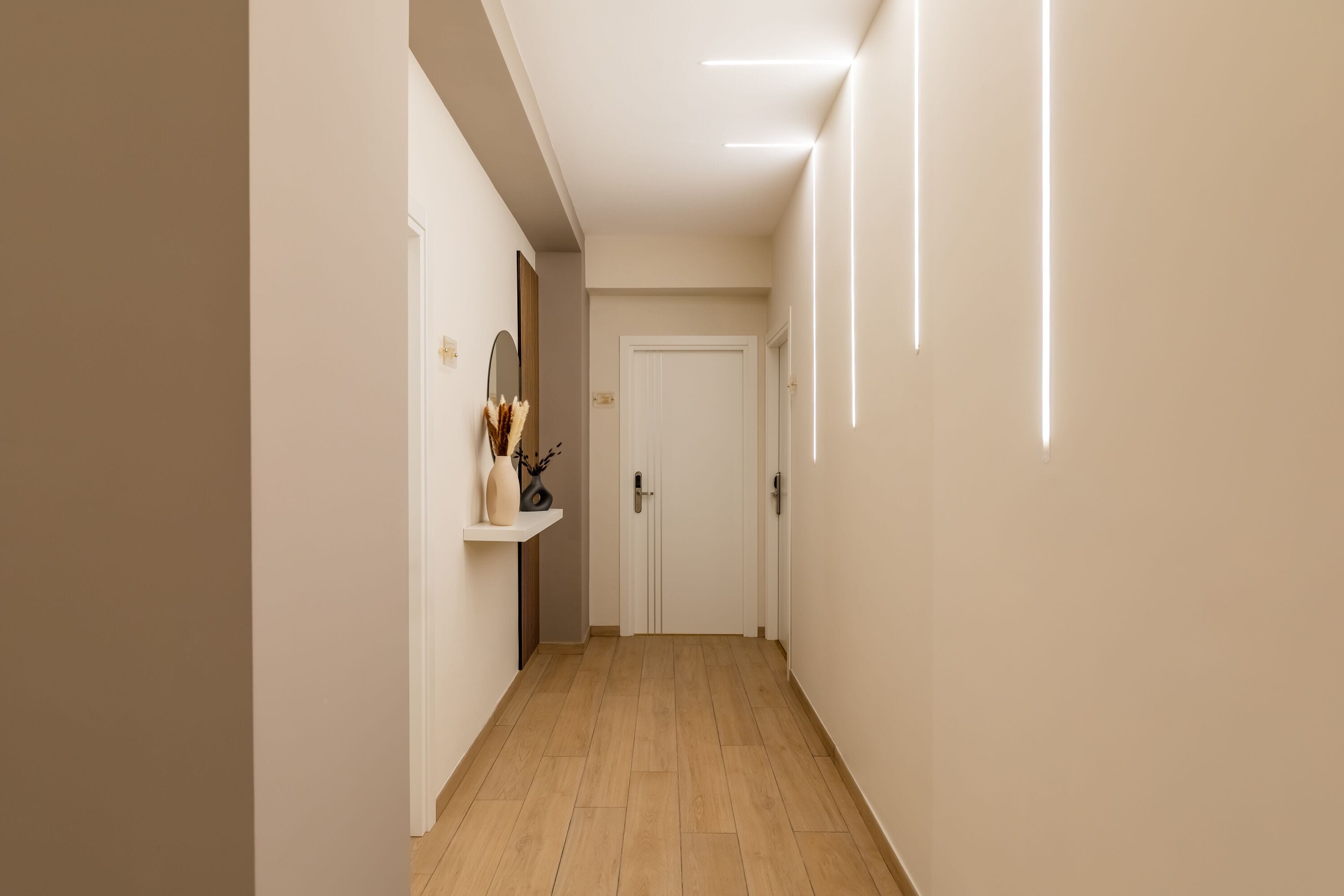 A narrow hallway with a wooden floor, white walls, and a door at the end.