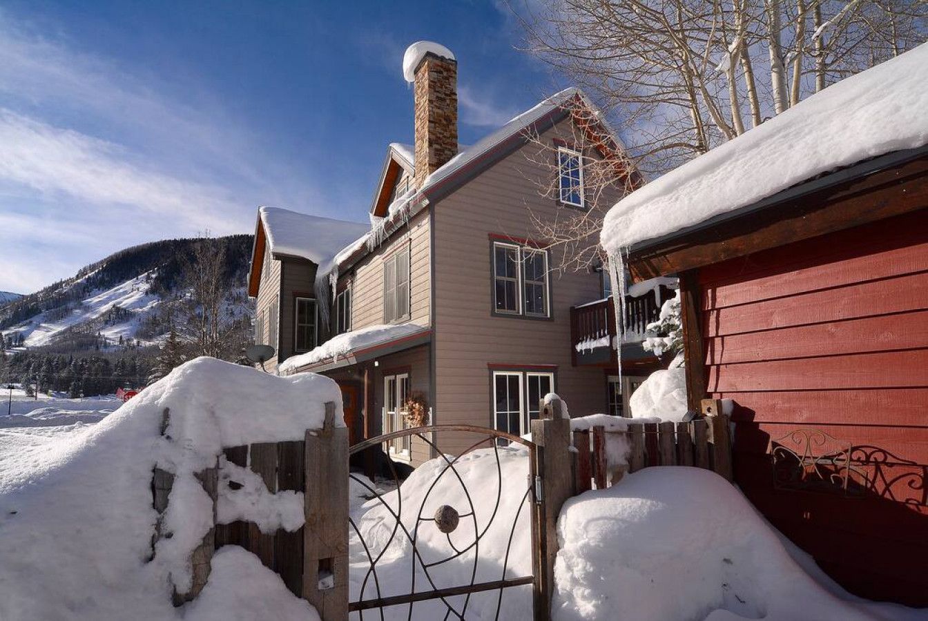 A two-story house with a chimney, a red exterior wall, and a snow-covered landscape.