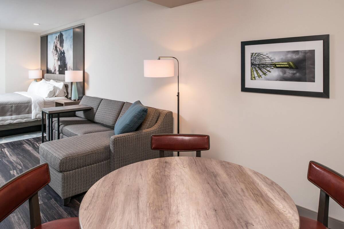 A hotel room with a bed, a sofa, a dining table, and a lamp.