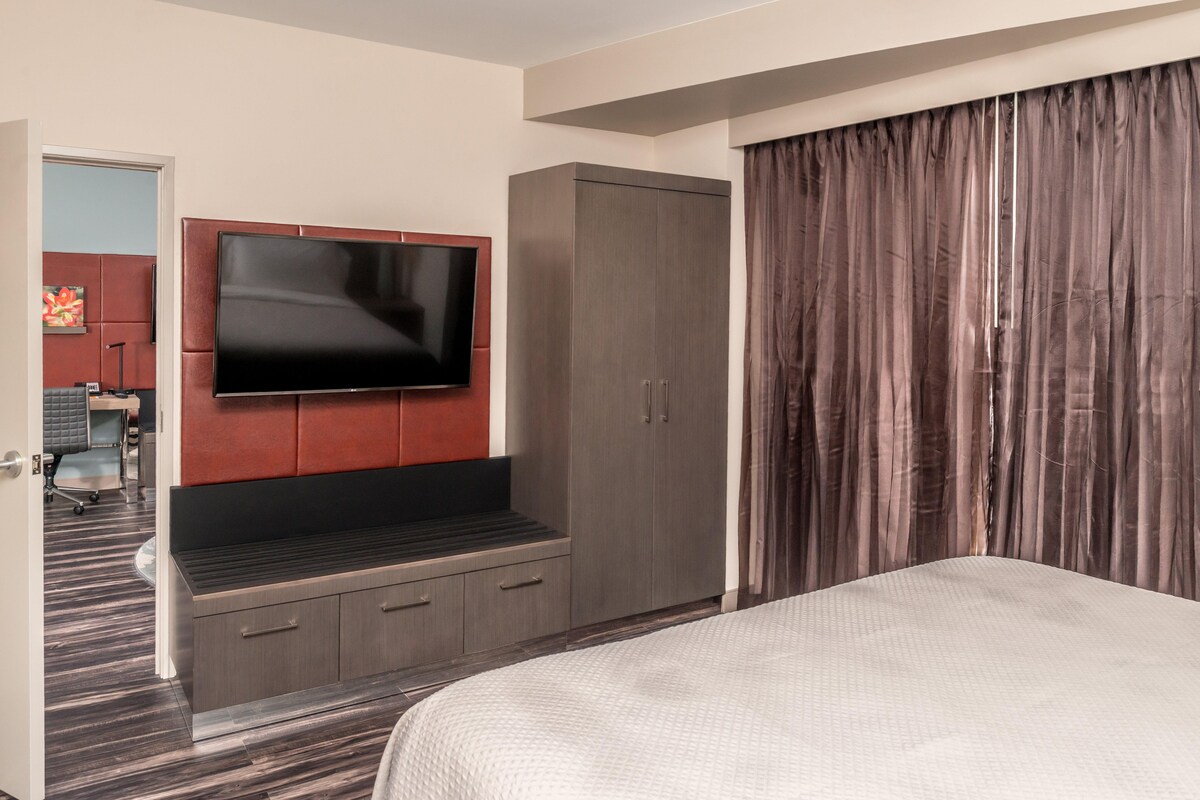 A hotel room with a large bed, a TV mounted on the wall, a wardrobe, and a door leading to a bathroom.