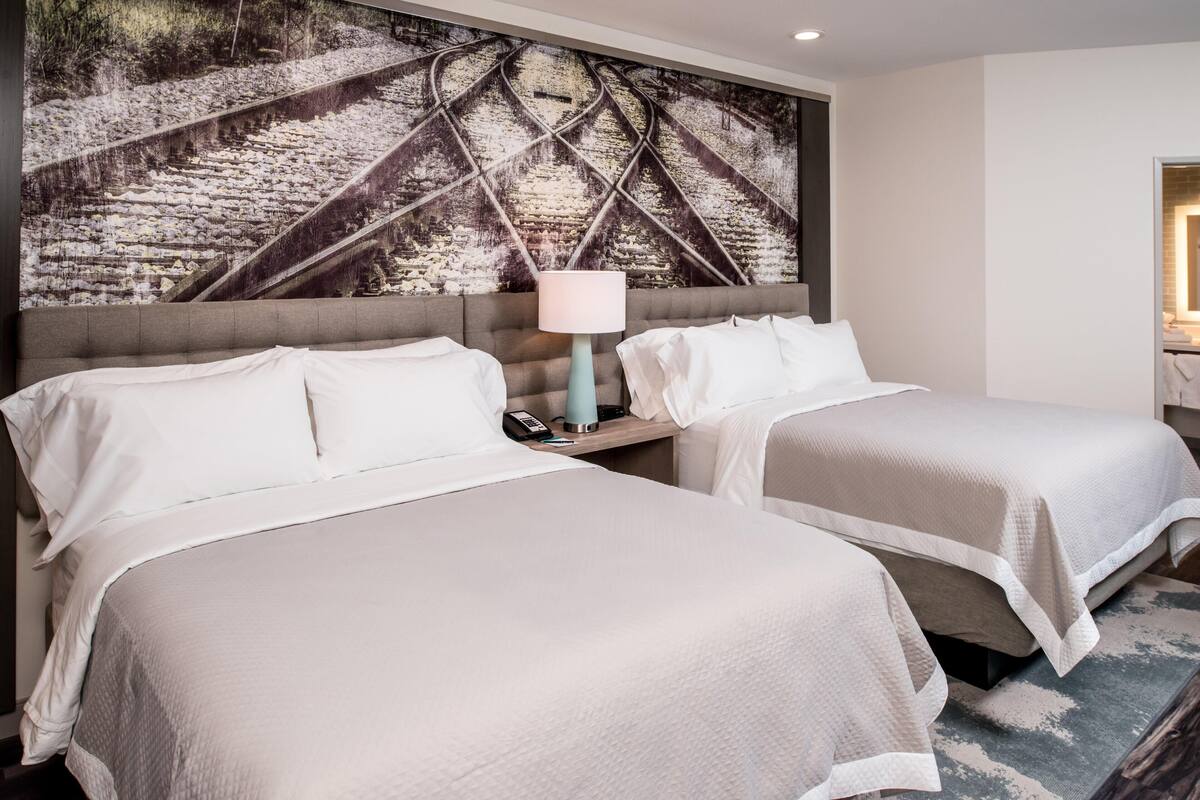 A hotel room with two beds, a large wall mural, a bedside lamp, and a nightstand.