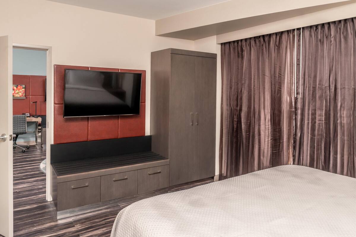 A hotel room with a large bed, a TV mounted on the wall, a wardrobe, and a door leading to a bathroom.