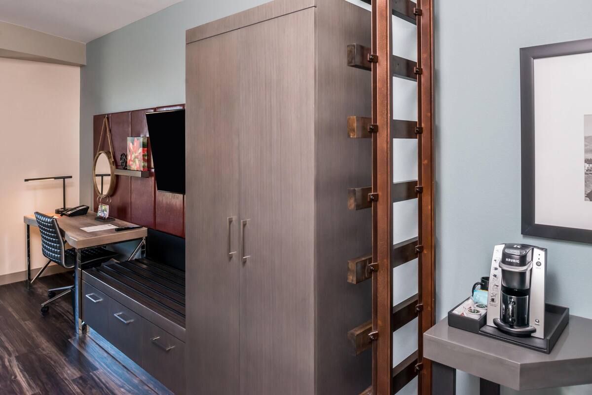 A room with a bed, a desk, a chair, a wardrobe, and a coffee machine.