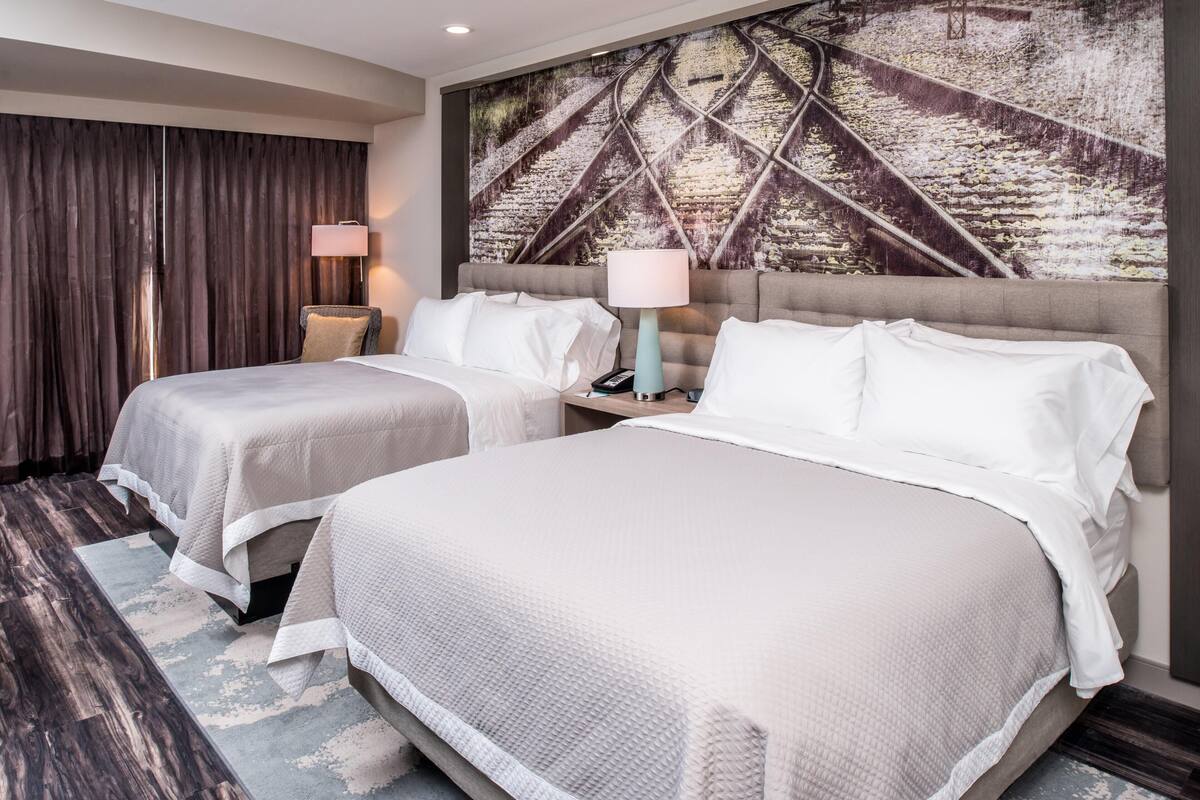 A hotel room with two beds, a large artwork on the wall, and a modern lamp.