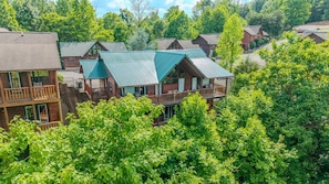 A multi-story log cabin with a green roof, surrounded by lush greenery.