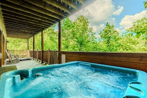 A hot tub under a wooden deck with a view of trees.