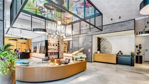A modern lobby with a curved reception desk, a piano, and a large window with a colorful view. - HYDE MIDTOWN RESIDENCES SPECTACULAR CORNER 2BR (Miami)