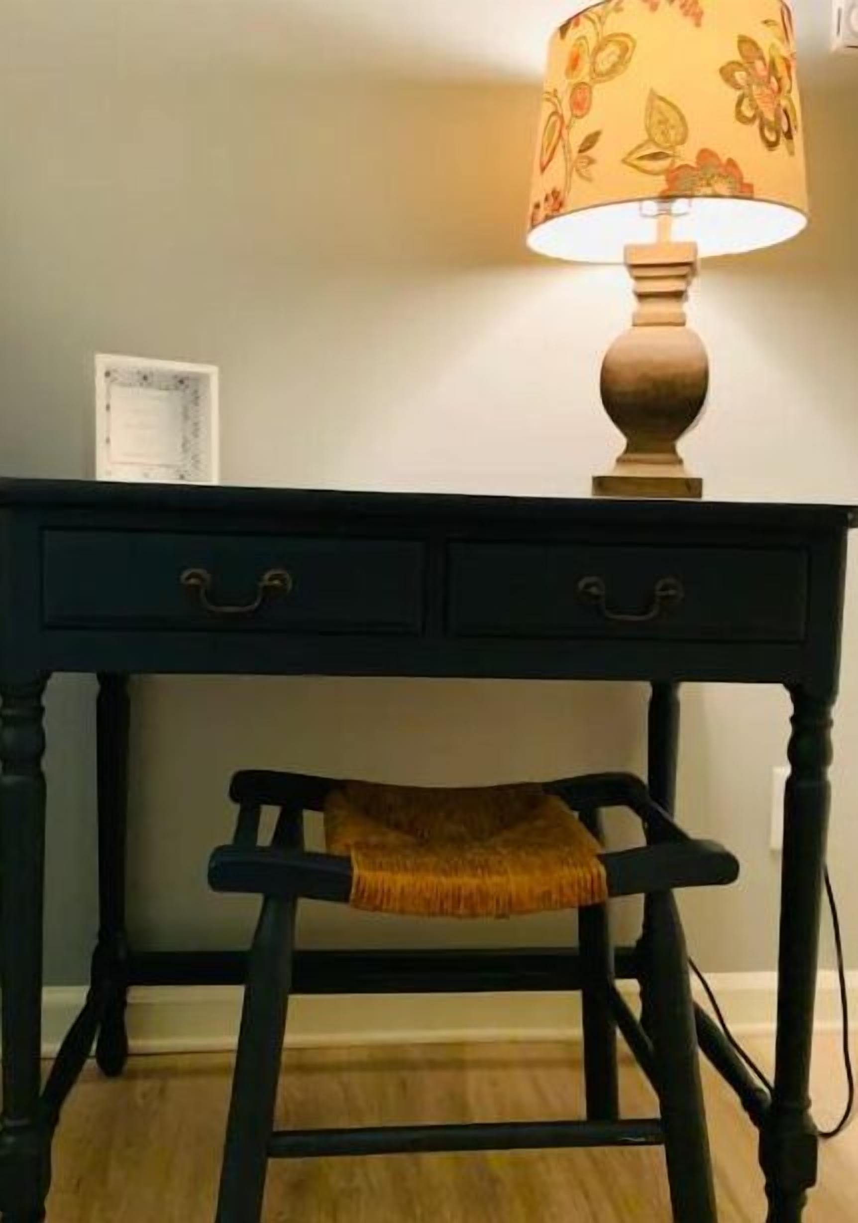 A dark wooden desk with two drawers and a lamp with a floral lampshade.