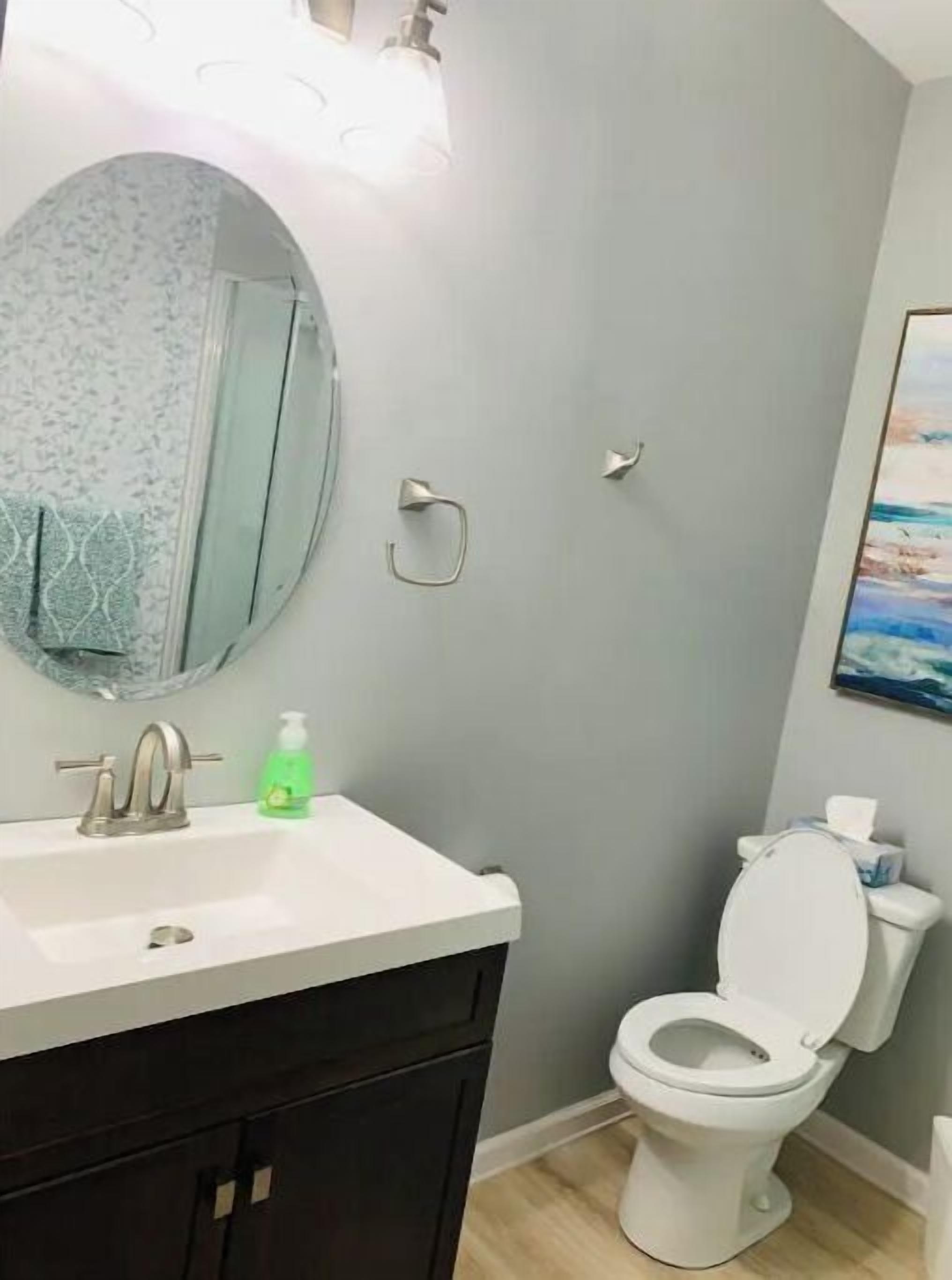 A bathroom with a white sink, a mirror, a toilet, and a painting on the wall.