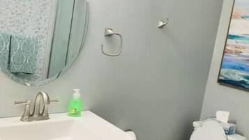 A bathroom with a white sink, a mirror, a toilet, and a painting on the wall.