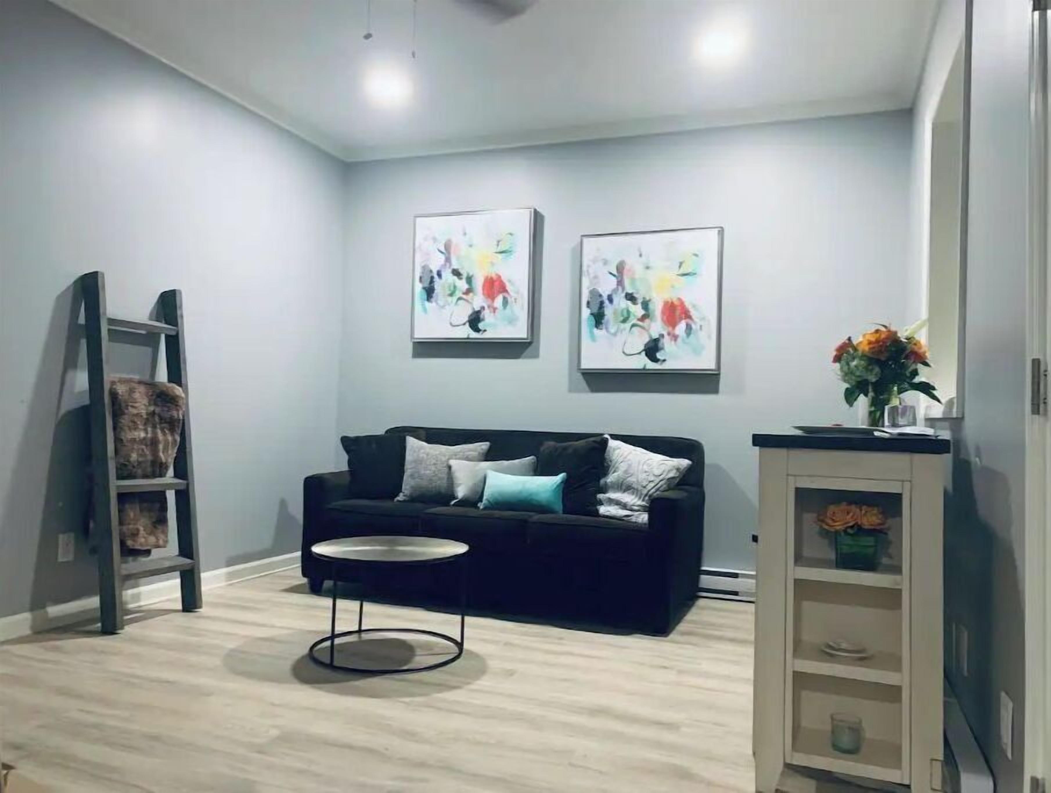 A modern living room with a black sofa, a round coffee table, and two abstract paintings on the wall.