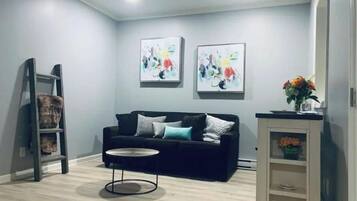 A modern living room with a black sofa, a round coffee table, and two abstract paintings on the wall.