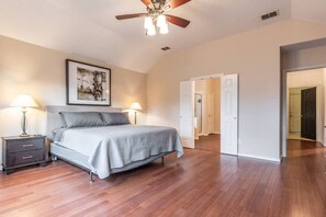 A bedroom with a bed, nightstands, a ceiling fan, and a door leading to another room.