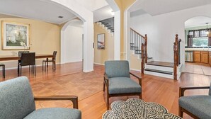 A spacious living area with a dining table, multiple chairs, a staircase, and a kitchen in the background.