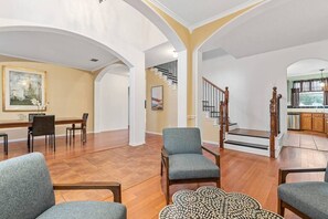 Un salón amplio con una mesa de comedor, varias sillas, una escalera y una cocina al fondo.