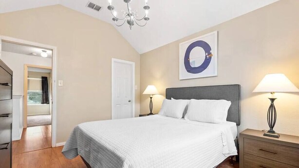 A bedroom with a large bed, two bedside tables with lamps, a wardrobe, a door leading to another room, and a wall with a circular decoration.