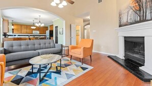A living room with a sofa, armchair, coffee table, fireplace, and a kitchen in the background.