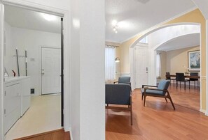 Amplia sala de estar con piso de madera, dos sillas azules, una mesa de comedor con sillas y una zona de cocina con lavadora y armarios.