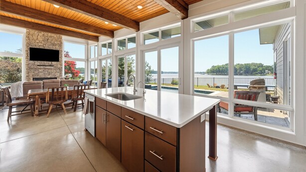 A spacious kitchen with a stone fireplace, large windows, and a view of a lake.