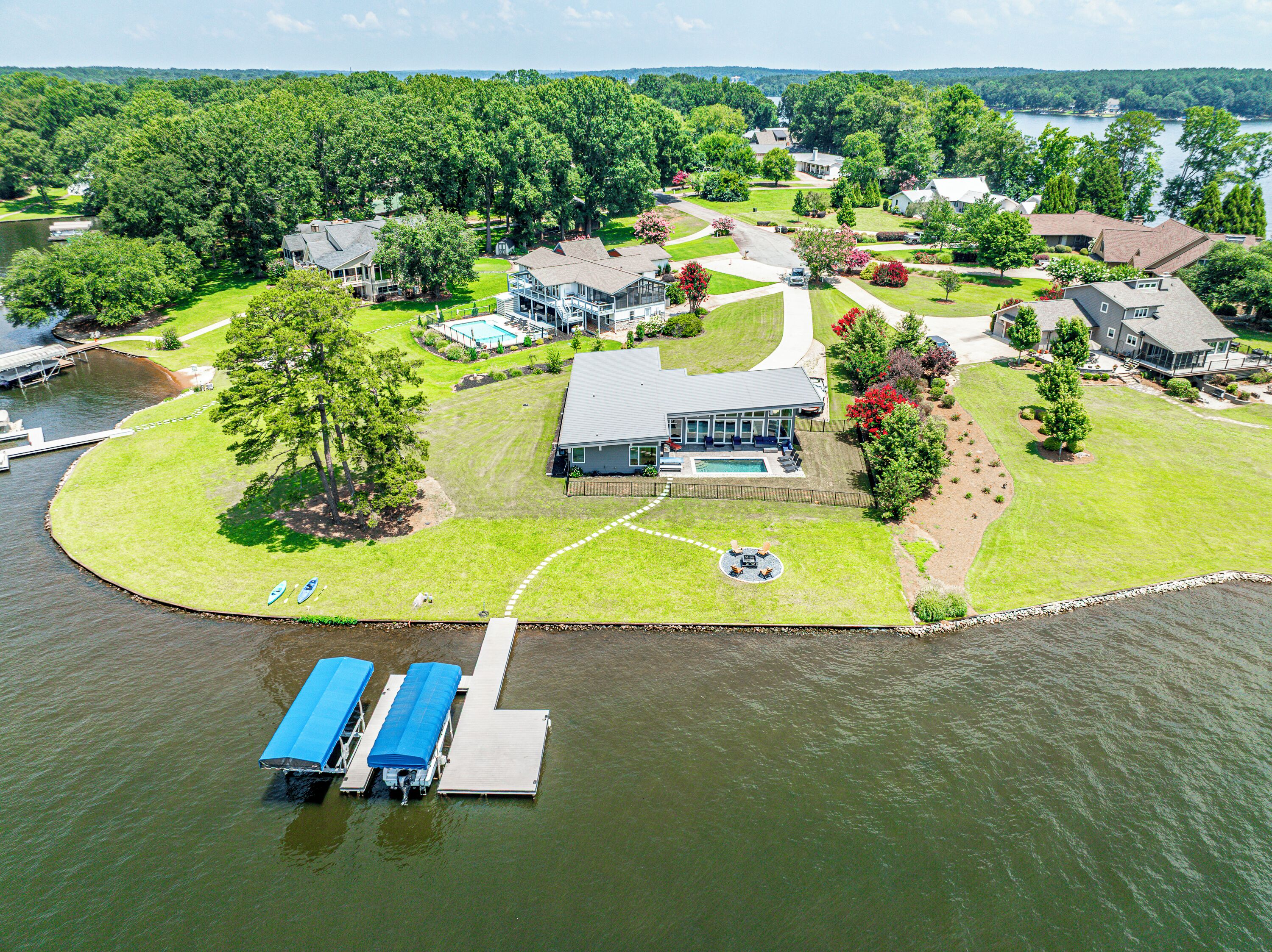 Une vue aérienne d’une propriété au bord du lac, avec une grande maison, un quai où sont amarrés des bateaux et une pelouse bien entretenue.