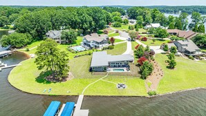 An aerial view of a lakeside property with a large house, a dock with boats, and a well-maintained lawn.
