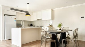 A modern kitchen with a central island, white cabinetry, and a dining area with clear chairs. - Balmain Family Tranquility - Harbour Views (Balmain East)