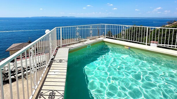 A clear blue sky, a swimming pool with a white railing, and a view of the ocean. - V021 - Neptuno (Roses)